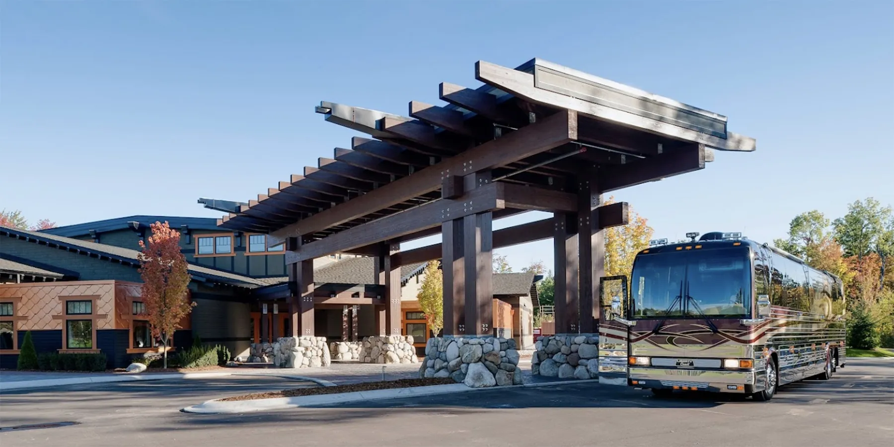 A rustic-style resort entrance featuring a grand wooden pergola with thick timber beams and stone pillars, providing a welcoming arrival experience.