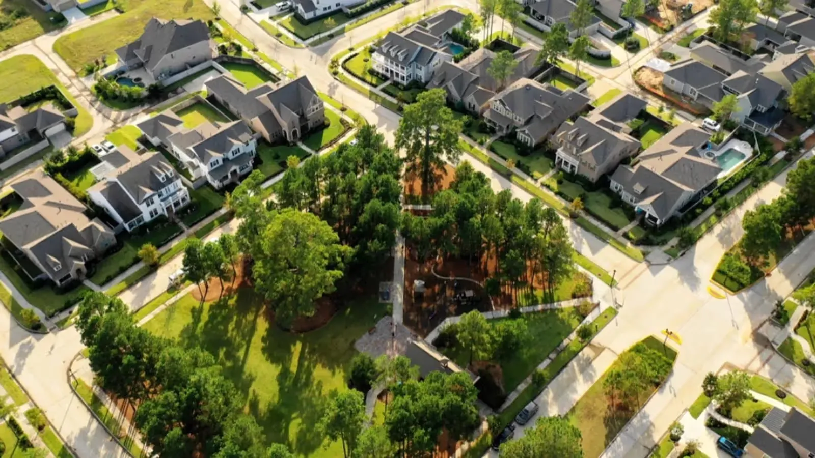 A large green park with a playground and a street view of a neighborhood.